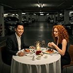 Couple dînant à une table dressée dans un parking souterrain, poisson d'avril