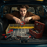 Homme assemblant une place de parking miniature dans son coffre, poisson d'avril