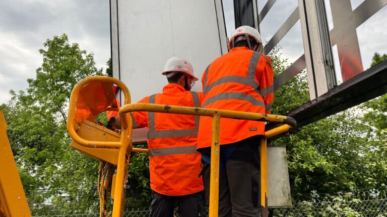 Techniciens en nacelle installant les modules LED d'un panneau